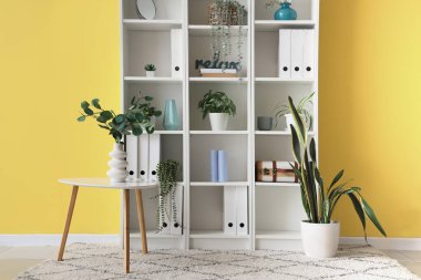 Ofisteki sarı duvarın yanında sehpa ve raf ünitesi.