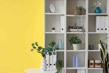 Ofisteki sarı duvarın yanında sehpa ve raf ünitesi.
