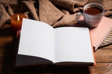 Kitaplı kış kompozisyonu, sıcak süveter ve kahverengi ahşap arka planda bir fincan çay.