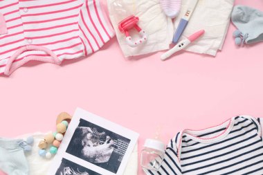 Bebek kıyafetleri, ultrason görüntüleri, hamilelik testleri ve pembe arka planda göğüs ucu şişeleriyle kompozisyon