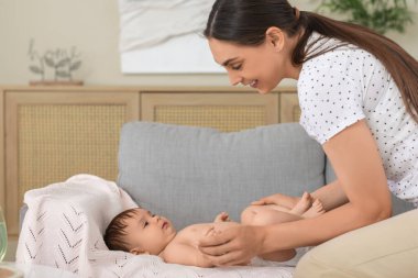 Anne evdeki kanepede bebeğinin bacaklarına masaj yapıyor.