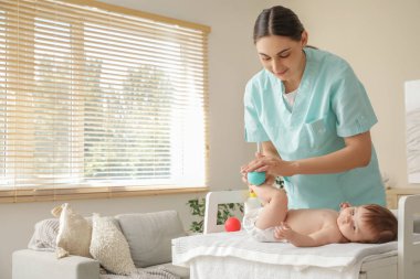 Sevimli küçük bebek, klinikteki koltukta oturan mutlu profesyonel terapistin topuyla bacak masajı yaptırıyor.