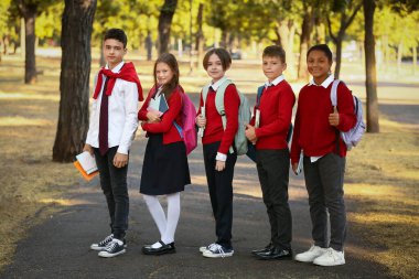 Açık havada okula giderken baş parmak hareketi yapan bir grup mutlu öğrenci.