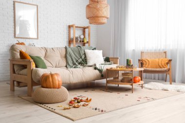 Sıcak kanepe, sehpa, koltuk, balkabağı ve sonbahar dekoru oturma odasının içinde.