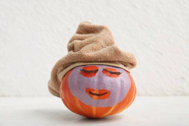 Takma kirpikli komik balkabağı, kozmetik maske ve arka planda havlu.