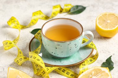 Kilo vermek için bir fincan çay, limon ve beyaz grunge masasındaki mezura, yakın çekim.