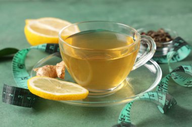 Kilo vermek için bir fincan çay, limon ve yeşil masadaki mezura, yakın plan.