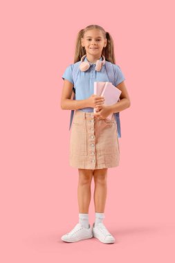 Okul üniformalı, pembe arka planda kitapları ve kulaklıkları olan sevimli bir kız.