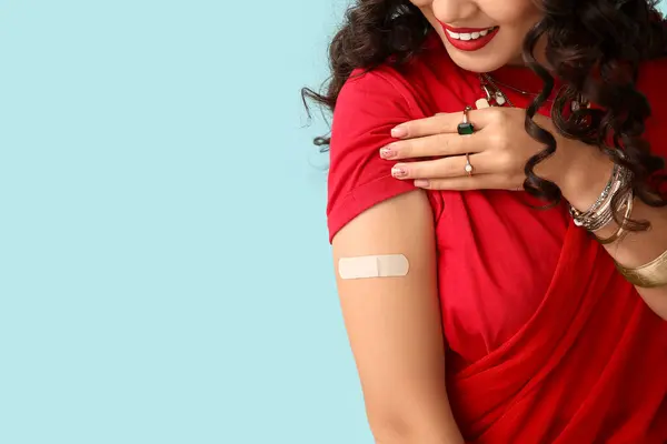 Beautiful Indian woman in sari with applied medical patch on blue background