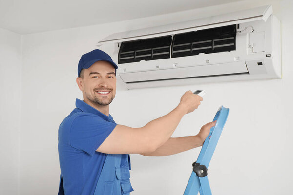 Male technician with remote control near air conditioner in room