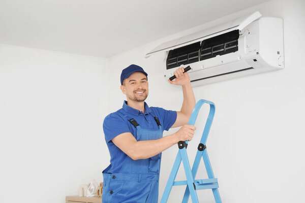 Male technician with flashlight checking air conditioner in room
