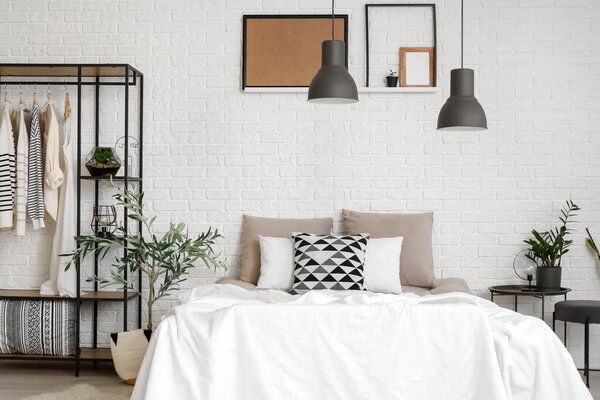 Modern bedroom with cozy bed, clothes rack and houseplant