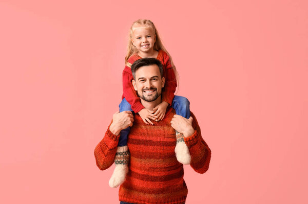 Happy father with his daughter in winter clothes on pink background