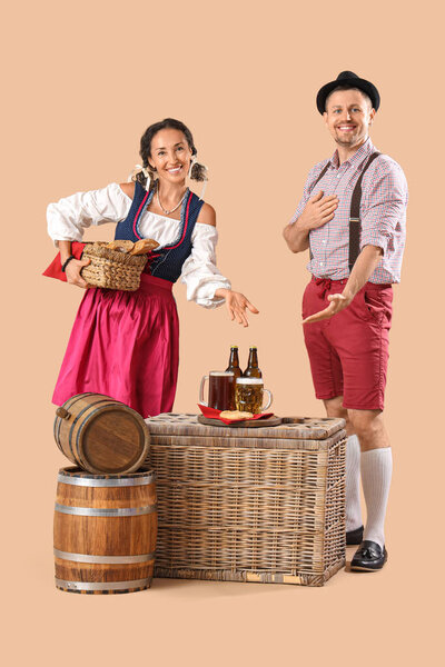 Happy mature waiters in traditional German clothes with barrels, mugs of beer and snacks on beige background