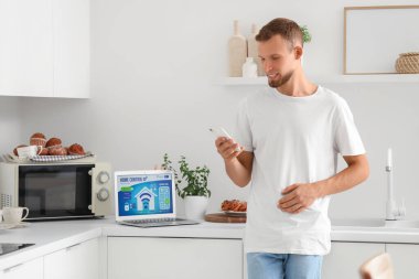 Genç adam mutfakta akıllı ev uygulaması olan cep telefonu kullanıyor.