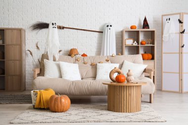 Cadılar Bayramı için dekore edilmiş oturma odasının içinde hayaletler, kanepe ve masa var.