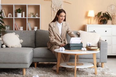 Güzel, mutlu, daktilo, kitap ve buruşuk kağıtlı bir kadın yazar evdeki kanepede oturuyor.