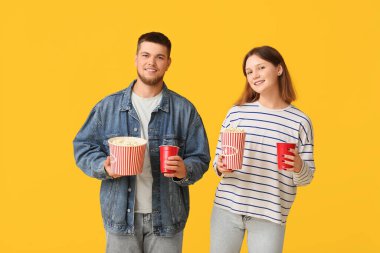 Patlamış mısır kovaları ve sarı arka planda bir bardak gazozu olan mutlu genç çift.