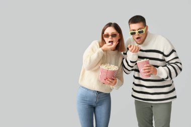 Üç boyutlu gözlüklü mutlu genç çift, gri arka planda patlamış mısır kovalarıyla