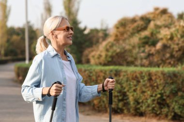 Güneş gözlüklü güzel olgun bir kadın parkta sırıklarla antrenman yapıyor.