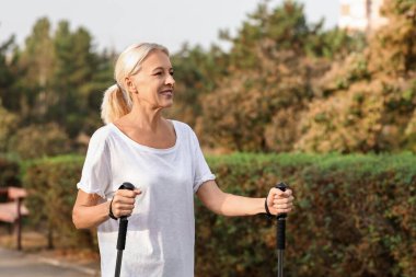 Güzel, olgun, mutlu bir kadın parkta sırıklarla antrenman yapıyor.