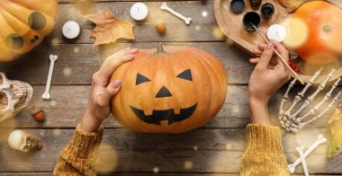 Ahşap masada Cadılar Bayramı balkabağı boyayan kadın.