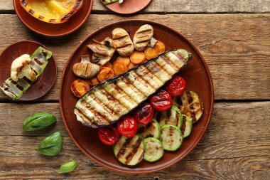 Izgara sebzeli tabaklar ve ahşap arka planda fesleğen.