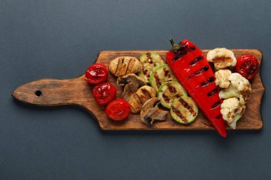 Gri arka planda ızgara sebzeli ahşap tahta.