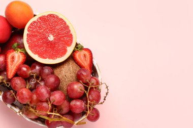 Hasır kase pembe arka planda farklı taze meyveler var.