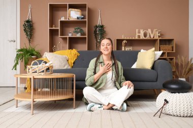 Glukofonlu genç bir kadın evde meditasyon yapıyor.