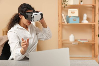 VR gözlüklü genç Afro-Amerikalı iş kadını. Masasında modern bir laptop var.