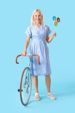 Oyuncak değirmeni ve mavi arka planda bisikleti olan olgun bir kadın.