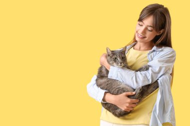 Sarı arka planda sevimli kedisi olan güzel, mutlu genç bir kadın.