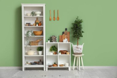 Mutfakta yeşil duvarın yanında bulaşık ve bitki bulunan modern raf ünitesi.