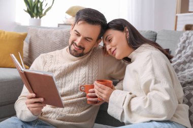 Sonbahar günü evde çay içip kitap okuyan genç bir çift.