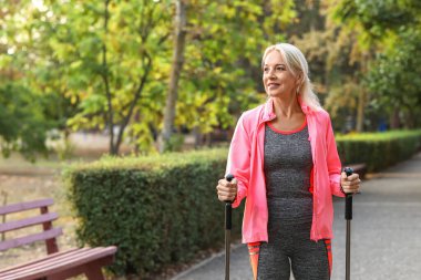 Güzel, olgun, mutlu bir kadın parkta sırıklarla antrenman yapıyor.
