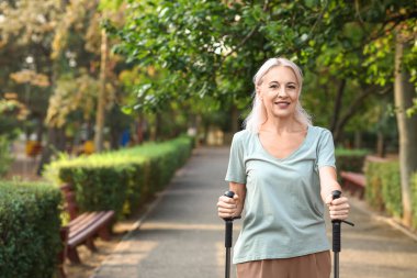 Güzel, olgun, mutlu bir kadın parkta sırıklarla antrenman yapıyor.