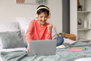 Kulaklıklı küçük çocuk yatak odasında dizüstü bilgisayar kullanıyor.