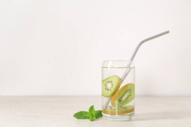 Beyaz zemin üzerinde kivi ve nane ile doldurulmuş su bardağı