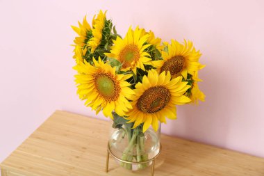 Vase with sunflowers on table near pink wall