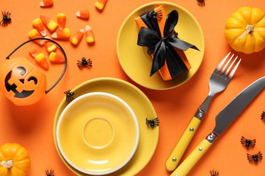 Cadılar Bayramı kutlaması için turuncu arka planda hediyeler, şekerler ve balkabaklarıyla şenlik masası.