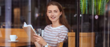 Genç kadın okuma kitabı kafede, camdan görüntülemek