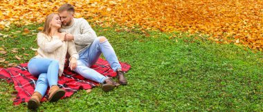 Sonbahar parkında ekose üzerinde oturan mutlu genç çift.