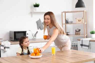 Annesiyle küçük bir kız mutfakta portakal suyu içiyor.