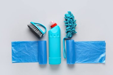 Bir şişe deterjan, çöp torbaları, mikrofiber paspas ve gri arka planda fırça.