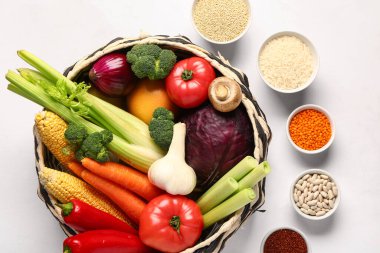 Farklı taze sebzeler ve beyaz arka planda mısır gevrekleri olan hasır bir kase.