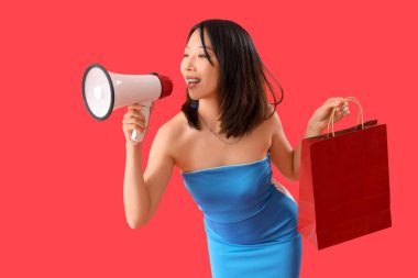 Güzel, mutlu, stil sahibi Asyalı kadın, alışveriş çantası ve kırmızı arka planda megafonla.