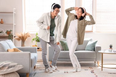 Kulaklıklı genç Asyalı arkadaşlar evde dans ediyor.