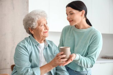 Yaşlı kadın mutfakta kızından bir fincan çay alıyor.