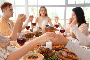 Şükran Günü 'nde şenlik masasında dua eden bir grup genç arkadaş.